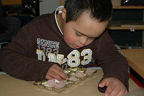 Ein Schüler beugt sich über eine Pralinenpackung, in der aus Gips hergestellte Schokolade liegt