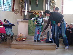 Schülerinnen, Schüler, Mitarbeiterinnen und Mitarbeiter der Schule unter den Eichen legen Dinge vor den Altar, für die sie Gott danken möchten.