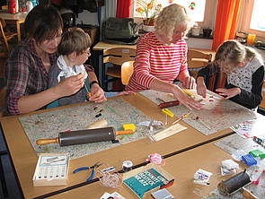 Schüler und Mitarbeiter sitzen am Tisch und stellen Perlen aus Fimo her.