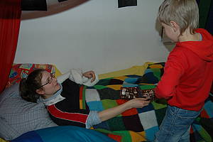 Ein Schüler überreicht der im Bett liegenden Erzieherin Schokolade