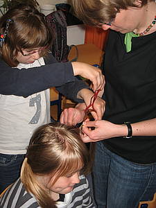 Eine Mitarbeiterin und eine Schülerin flechten einer anderen Schülerin Zöpfe.