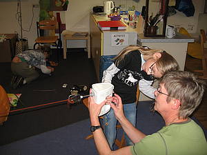 Eine Schülerin und eine Mitarbeiterin beugen sich über ein Handrührgerät, an dem Wolle befestigt ist, die zu einer Kordel gedreht werden soll.